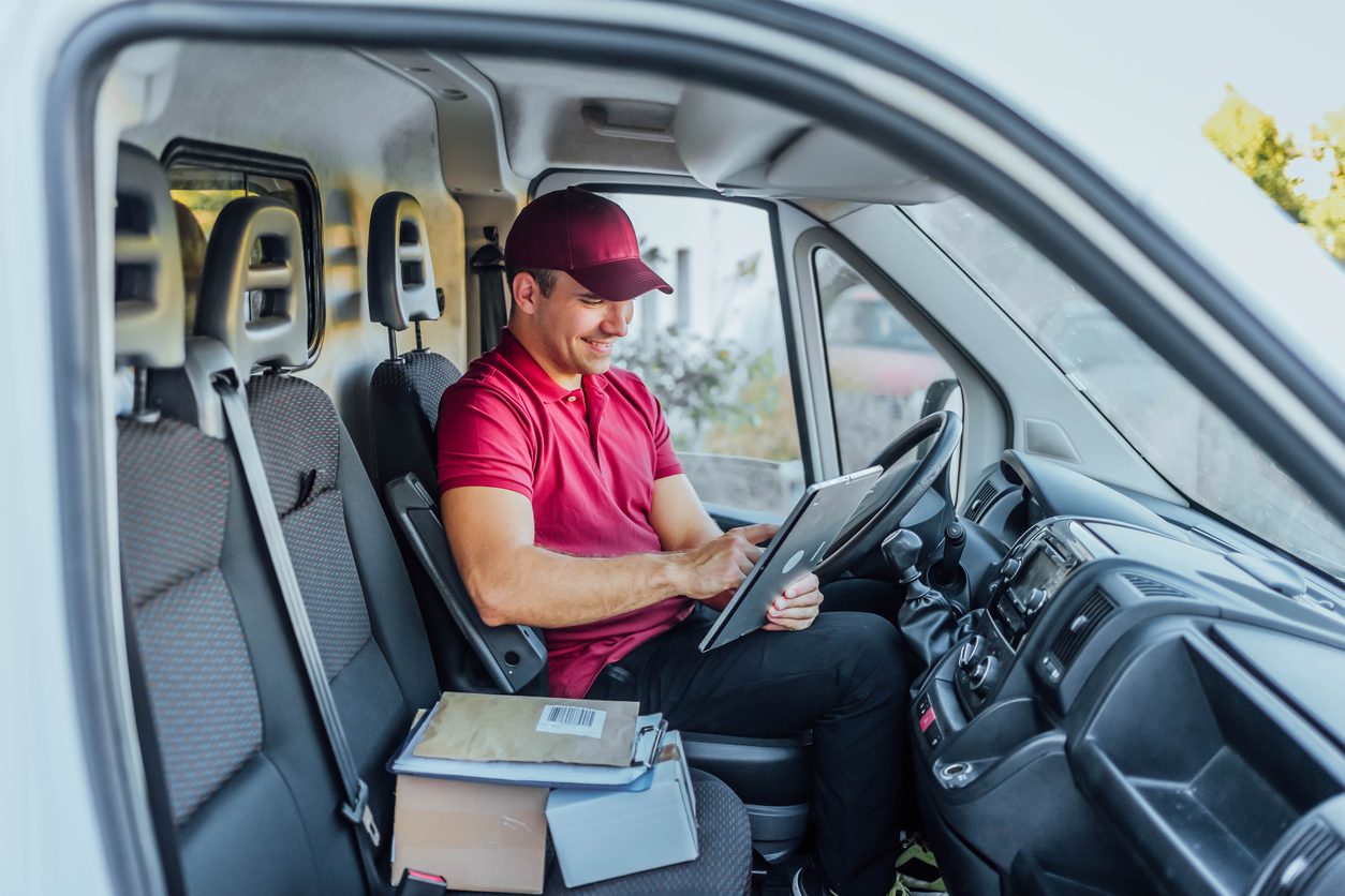 A food delivery person sits in truck using a tablet to access route optimization software.